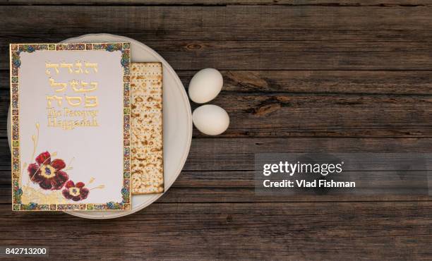 white plate  with matzah or matza and passover haggadah on a vintage wood background presented as a passover seder feast or meal with copy space. - passover seder plate stock pictures, royalty-free photos & images