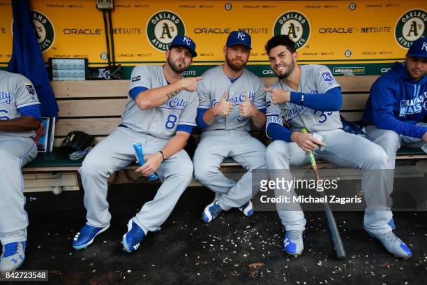 Mike Moustakas, Brandon Moss and Eric Hosmer of the Kansas City Royals sit in the dugout prior to the game against the Oakland Athletics at the...