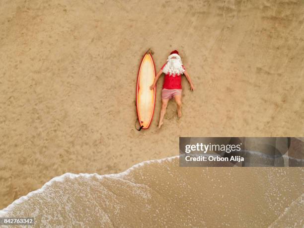 santa claus mit surfbrett - beach christmas stock-fotos und bilder