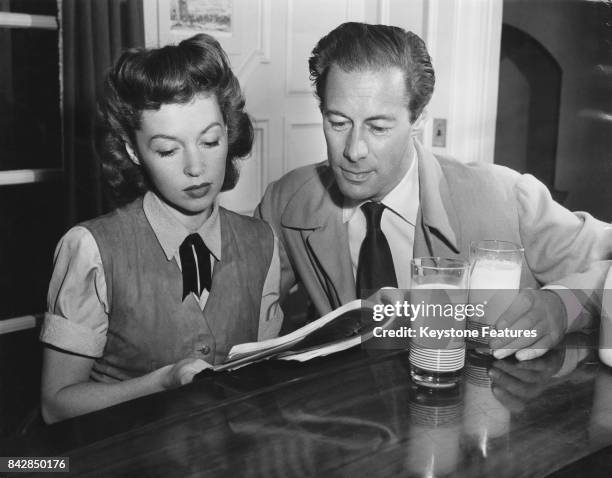 American actor Rex Harrison reading a script with his wife, actress Lilli Palmer over glasses of milk, May 1948.