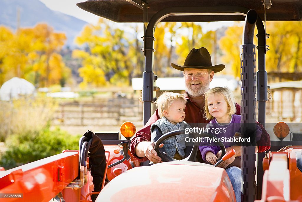 Toddler children & farmer riding on tractor.