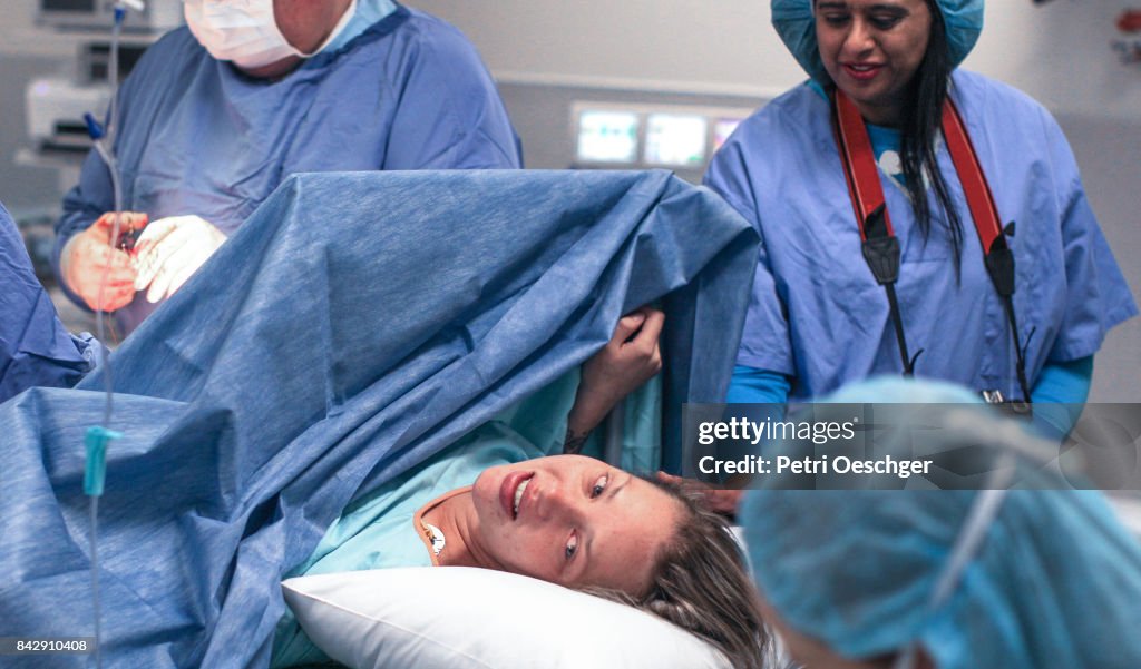 A Doula supports and comforts her emotional pregnant client as she lays in the operating theatre.