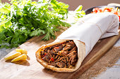 Shawarma ; Grilled Lamb Kebab Doner Wrap with yogurt, pickel, onion, aubergine and tomato on rustic white painted rustic wood table.