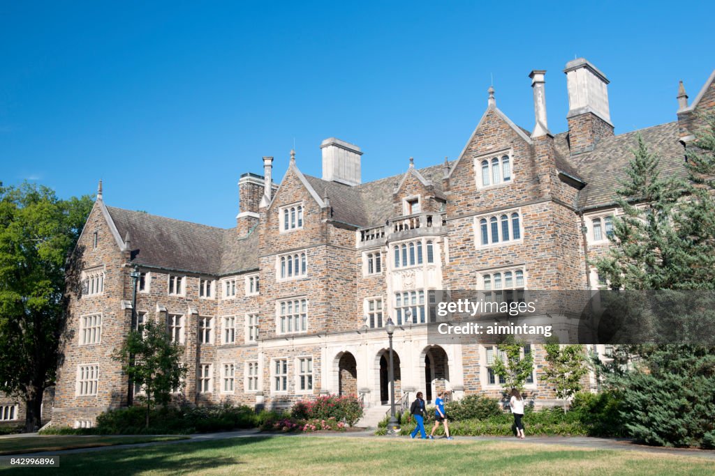 Three female students walking past a dorm building in the campus of Duke University