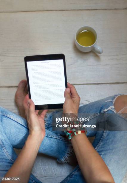 mujer en jeans apenado se relaja con tabletas y té - fashion woman floor cross legged fotografías e imágenes de stock