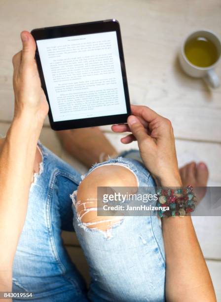 mujer en jeans apenado se relaja con tabletas y té - fashion woman floor cross legged fotografías e imágenes de stock