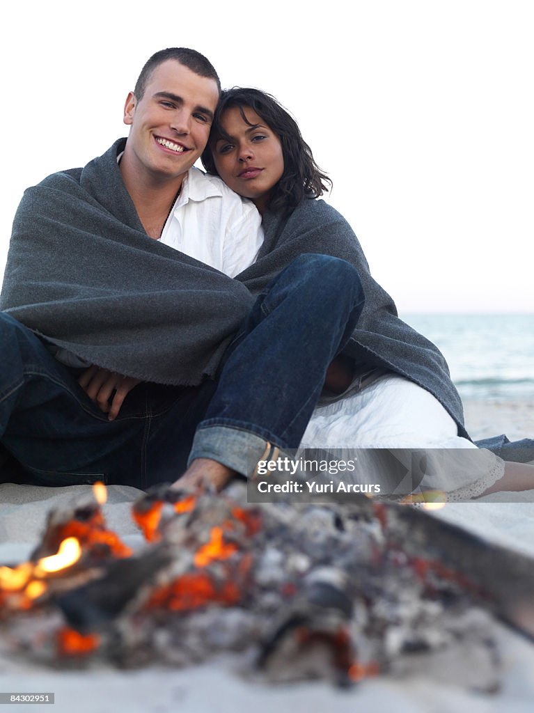 Young couple relaxing by campfire on beach