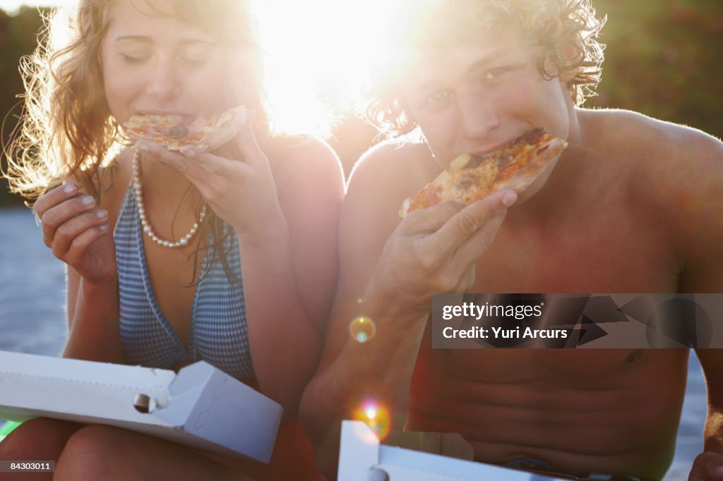 Young couple eating pizza on beach