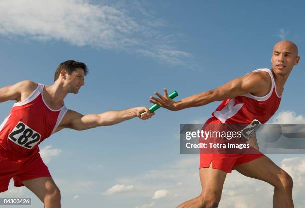 runner passing baton to teammate - staffel stock-fotos und bilder