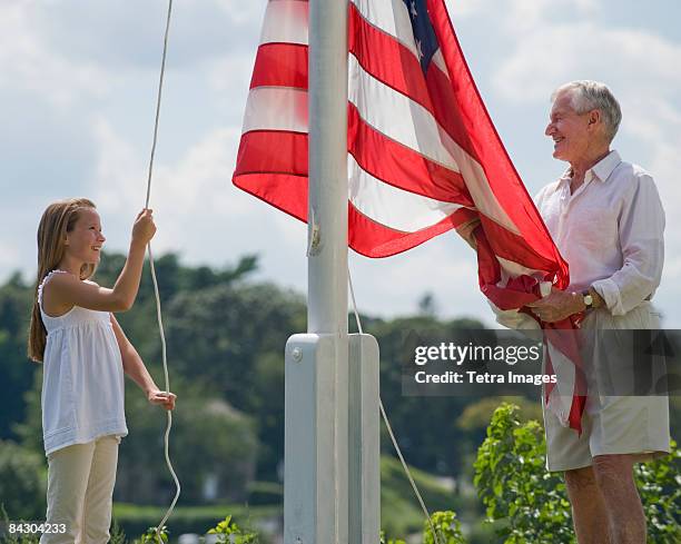 grandfather and granddaughter raising american flag - flagpole stock-fotos und bilder