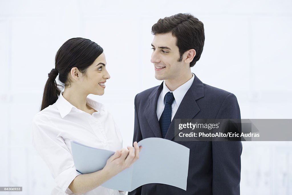 Professional woman showing male colleague document, both smiling