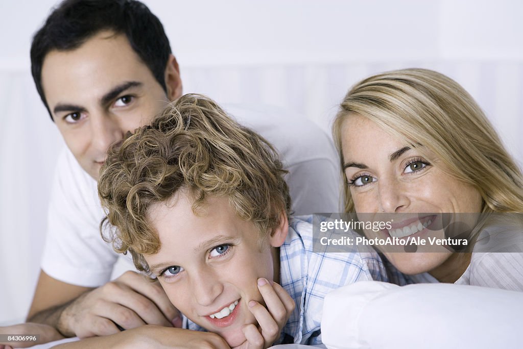 Young boy relaxing with his mother and father, all smiling at camera