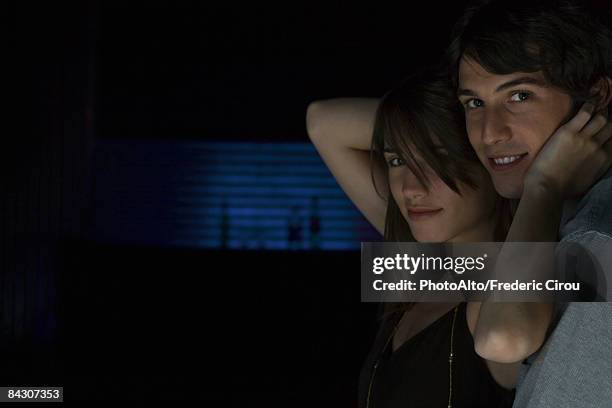 couple close together, smiling at camera, woman raising arms to touch man's face - couple dark background stock-fotos und bilder