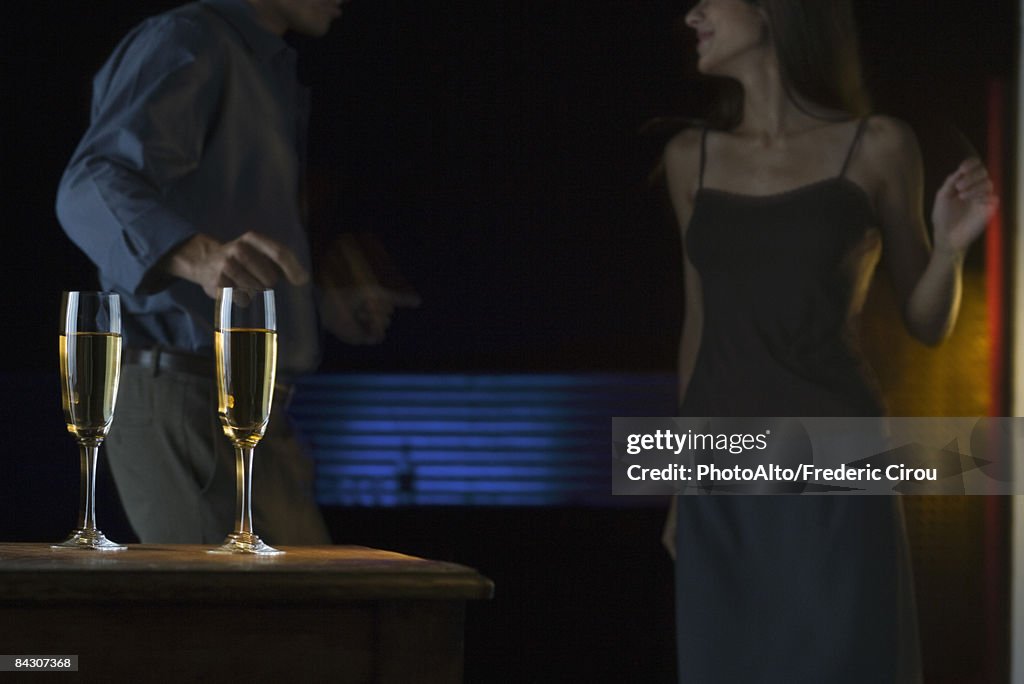 Glasses of champagne, couple dancing in darkly lit background