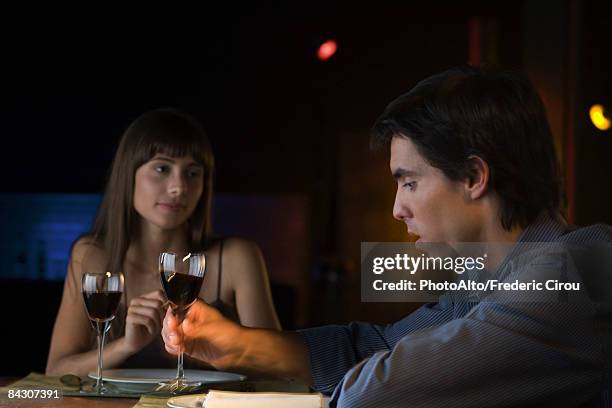 couple having serious conversation over dinner at restaurant, man picking up glass of wine - couple dark background stock-fotos und bilder