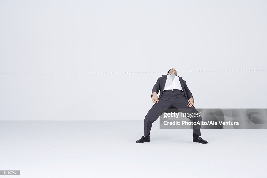 Businessman doing limbo, bending backwards to go under rope