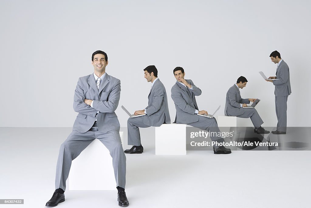 Businessman smiling at camera with arms folded while his clones use laptops in background