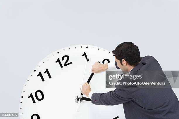 businessman pushing back hands of clock - corsa contro il tempo foto e immagini stock