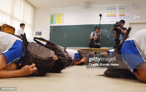 Elementary school students hold their heads and keep their bodies low during an emergency drill in the western Japan town of Okinoshima on Sept. 6 in...