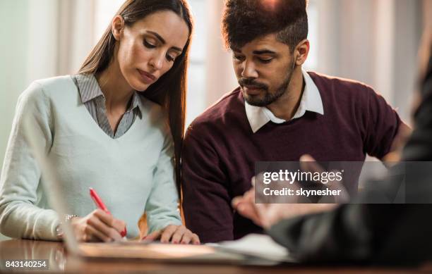 young couple signing a contract on a meeting with insurance advisor. - couple signing stock pictures, royalty-free photos & images