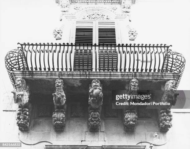 Italy, Sicily, Noto, Nicolaci palace. Whole artwork view. Stone corbel sculpted woth grotesques sustaining a balcony with curved grating.