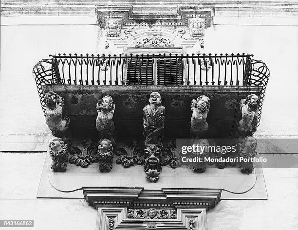 Italy, Sicily, Noto, Nicolaci palace. Whole artwork view. Stone corbel sculpted woth grotesques sustaining a balcony with curved grating.