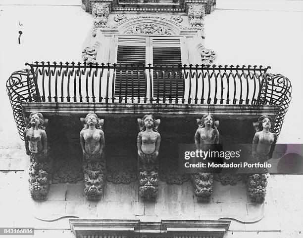 Italy, Sicily, Noto, Nicolaci palace. Whole artwork view. Stone corbel sculpted woth grotesques sustaining a balcony with curved grating.