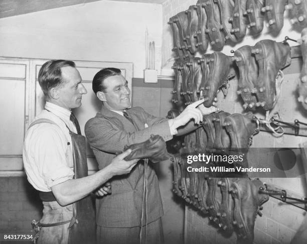 English footballer Eddie Hapgood , captain of Arsenal F.C., discusses football boots with 'Cobbler' Lee, the team's shoe-maker, at Highbury, London,...