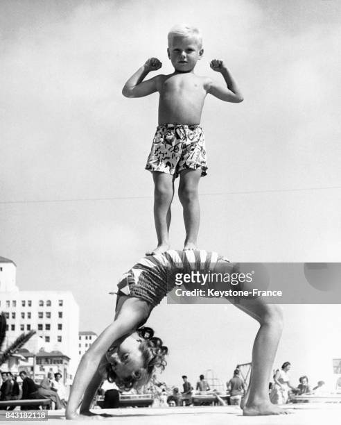 Petit Tarzan debout sur le ventre de sa soeur qui fait le pont, sur la plage de Santa Monica, Californie, Etats-Unis.