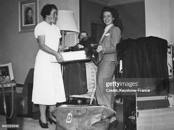 Danielle Darrieux, en partance pour Hollywood, faisant ses bagages, aidée par son employée de maison, dans son appartement à Paris, France, le 24...