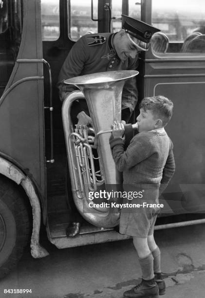 Un chef de fanfare aide un enfant à mettre son tuba dans le bus tandis que ce dernier souffle dedans.