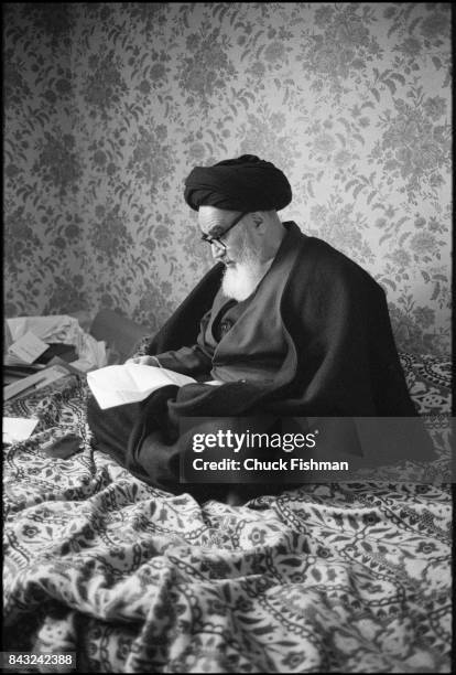 While living in exile, Iranian religious and political leader Ayatollah Ruhollah Khomeini sits cross-legged and reads a letter, Neuphe-le-Chateau,...