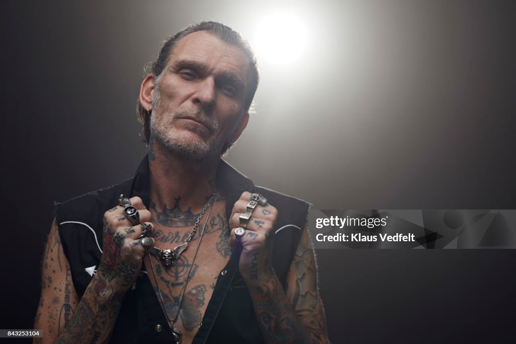 Tattoed mid aged man wearing lots of finger rings and looking in camera