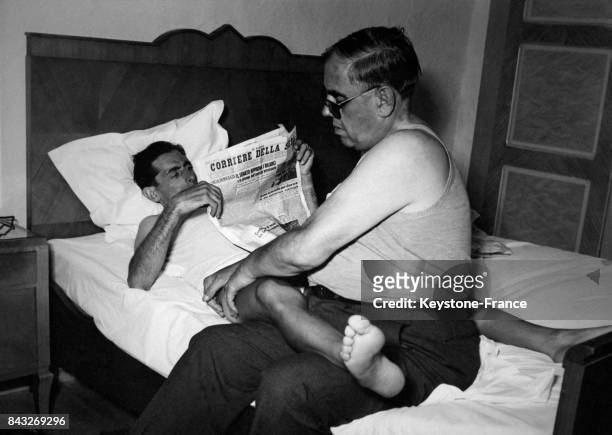 L'hôtel entre deux étapes, Fausto Coppi lit le journal allongé dans son lit tandis que le soigneur de l'équipe lui masse les cuisses, en Italie en...