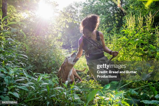 woman in fishing gear with her staffordshire bull terrier dog outdoors - butter curl stock-fotos und bilder