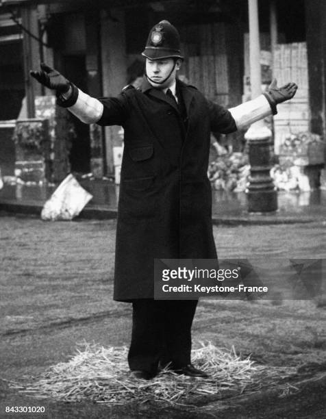 Agent de la circulation à un carrefour de la capitale est debout sur du foin pour réchauffer ses pieds, à Londres, Royaume-Uni en janvier 1962.
