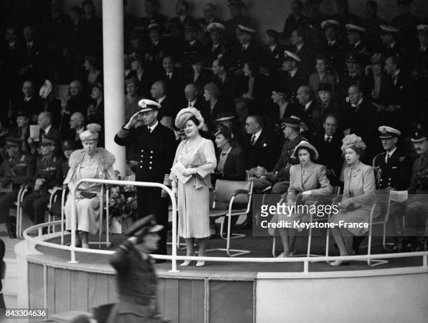 Le Roi George VI salue le défilé des troupes britanniques depuis la tribune en compagnie de sa mère la Reine Mary, de sa femme la Reine Elizabeth et...