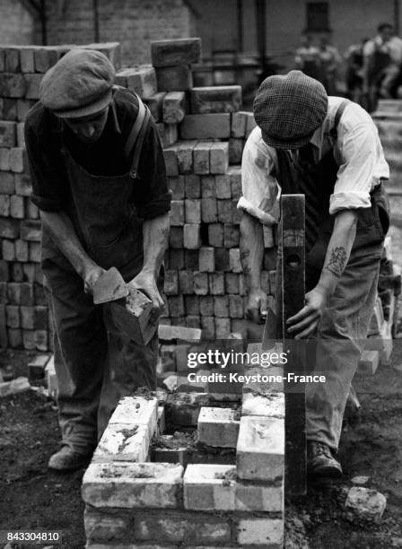 Deux ouvriers travaillant à la reconstruction de la capitale britannique montent des parpaings d'une cheminée, à Londres, Royaume-Uni circa 1940.