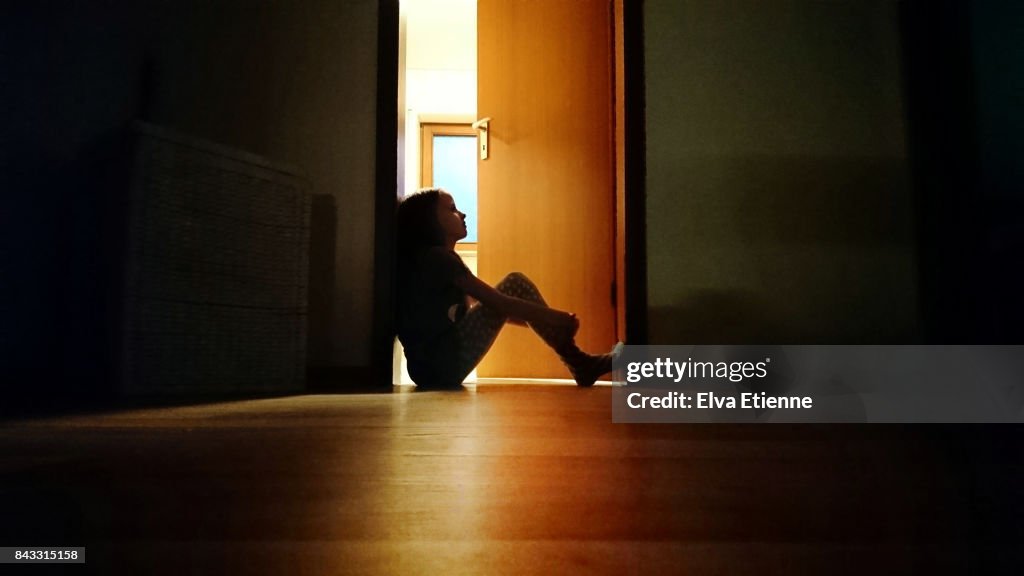 Backlit child sitting in a dark doorway in contemplation