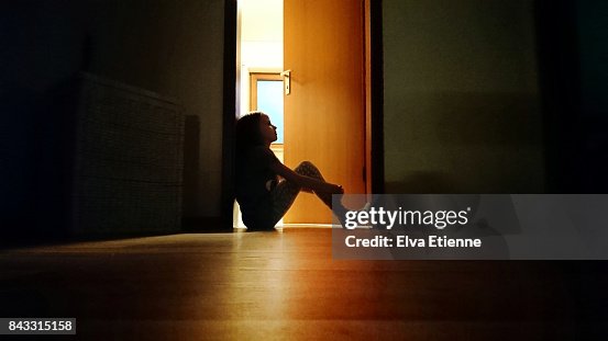 Backlit child sitting in a dark doorway in contemplation Backlit child sitting in a dark doorway in contemplation