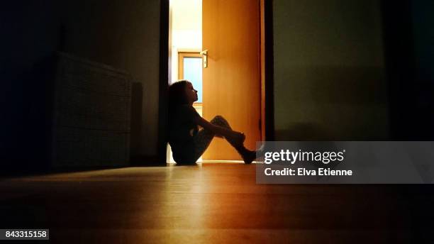 backlit child sitting in a dark doorway in contemplation - one girl only stock pictures, royalty-free photos & images