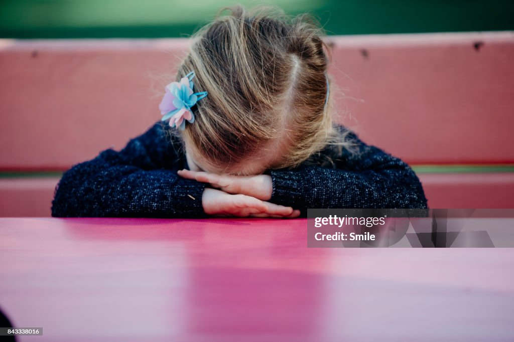 Young girl with head on hands sitting at pink table