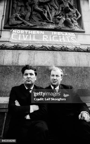 Portrait of Irish politicians John Hume and Ivan Cooper as the pose together at the base of Nelson's Column in Trafalgar Square, under a sign that...