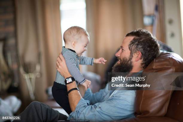 bearded man in recliner holding laughing baby - recliner chair stock pictures, royalty-free photos & images