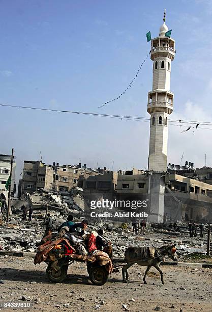 Palestinians carry their belongings on a donkey cart as they leave the area while they pass by the rubble of the Taha mosque after it was struck by...