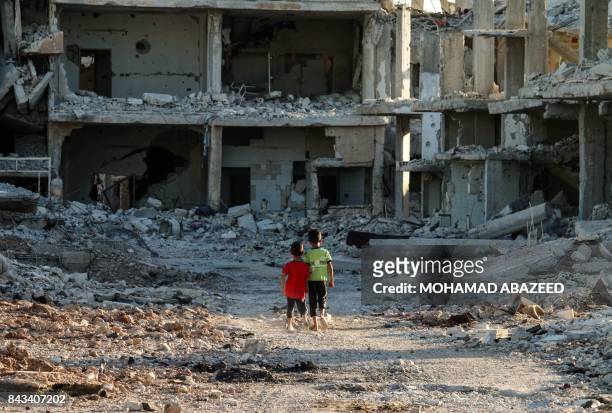 Two Syrian boys walk down a street amid destroyed buildings in a rebel-held area in the southern Syrian city of Daraa, on September 6, 2017.