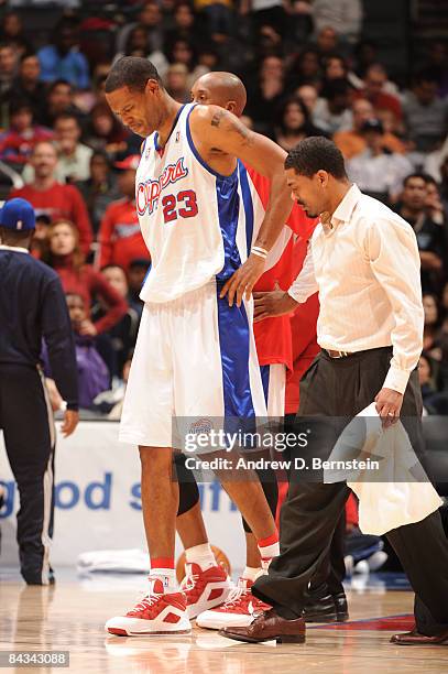 Marcus Camby of the Los Angeles Clippers walks off the court with head athletic trainer Jasen Powell after sustaining a right ankle injury during a...