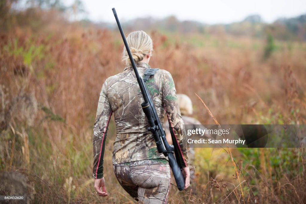 Blond Mother with Rifle Walking in Field with Child Running Ahead