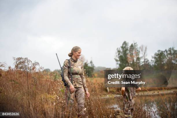 smiling mother with rifle gun slung on her shoulder facing her child in tall grass - hunter brown stock pictures, royalty-free photos & images