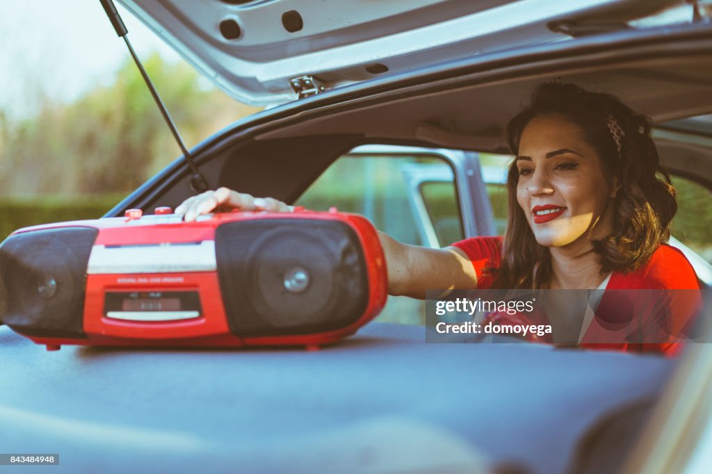Young woman playing music on a boom box from a car
